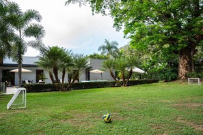 A grassy area with a soccer goal, palm trees, and a building with outdoor seating. - Luxury Villa in Santa Fe de Antioquia (Casa Sereno) (San Nicolas)
