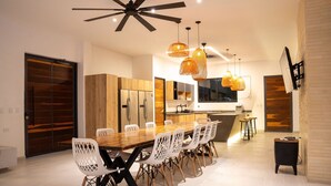 Een moderne keuken met een centraal eiland, houten keukenkastjes en een eethoek met een lange tafel en witte stoelen.