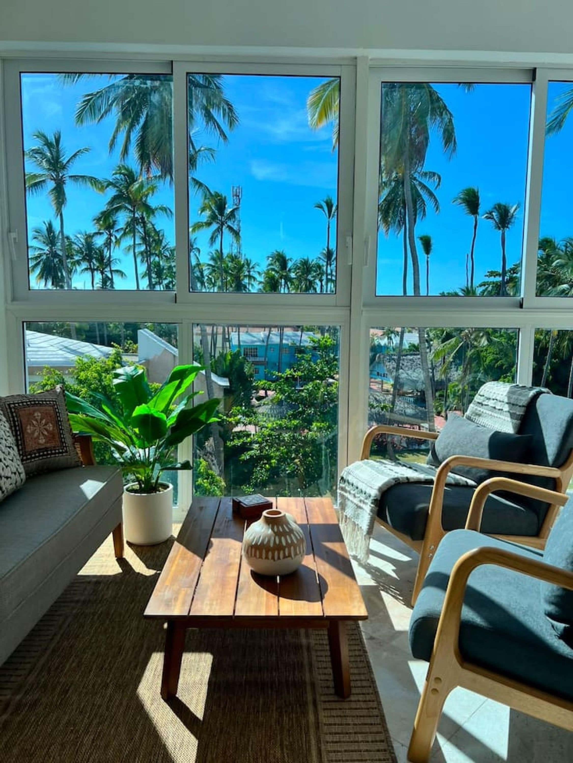 A room with a large window, a wooden table, a sofa, and a potted plant.