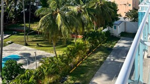 A view of a beachfront property with palm trees, a pool, and a clear blue sky. - Beachfront Penthouse w Rooftop Pools Views (Punta Cana)