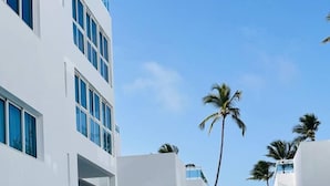 A modern hotel with a swimming pool, palm trees, and a view of the ocean. - Beachfront Penthouse w Rooftop Pools Views (Punta Cana)