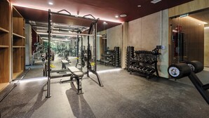 Un gimnasio con equipo de levantamiento de pesas, bancos y un espejo grande.