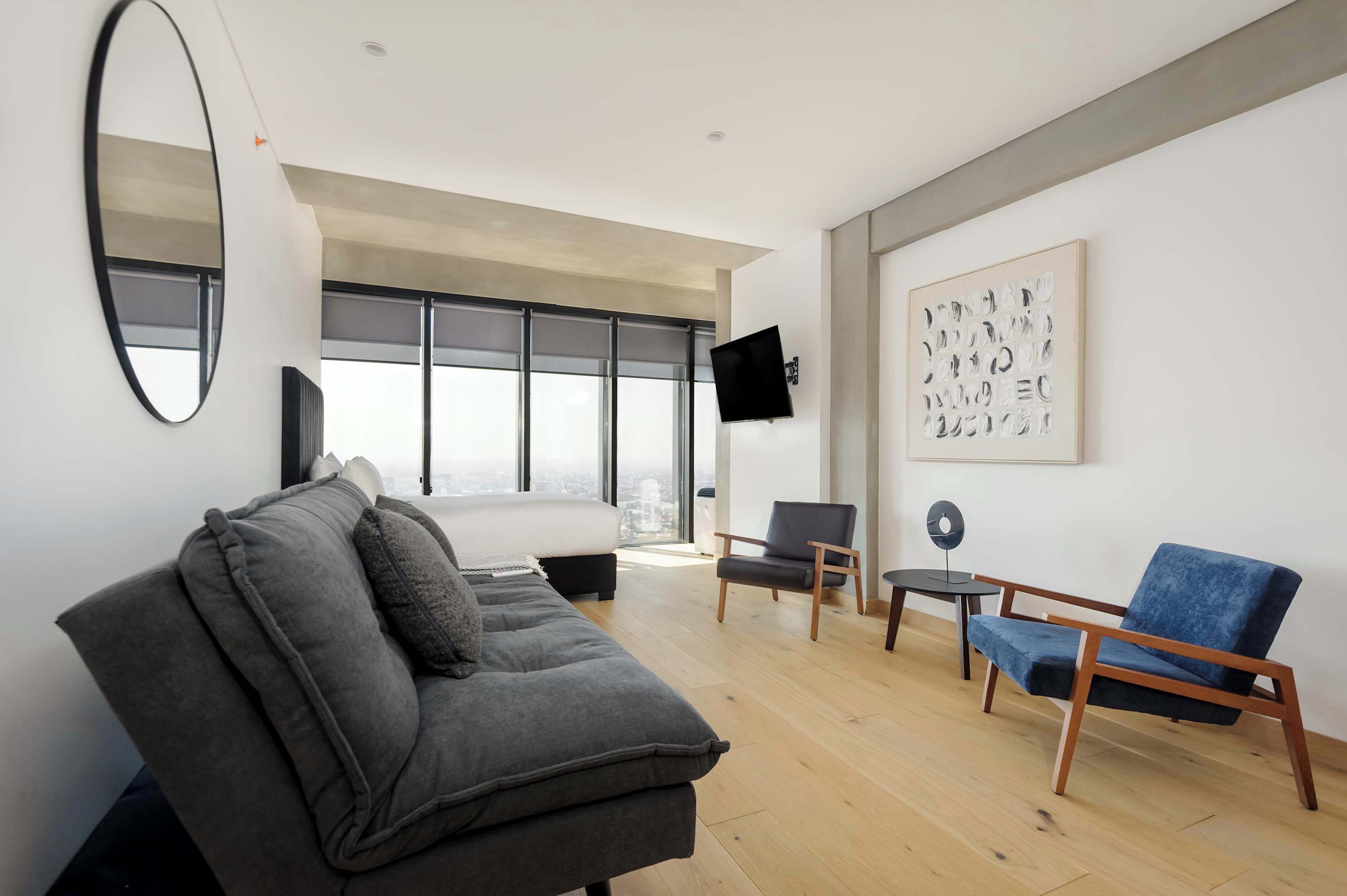 A modern living room with a grey sofa, a blue armchair, a flat-screen TV, and a large abstract painting on the wall.