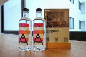 Zwei Flaschen 'sin-gas' mit einem QR-Code und einer Broschüre mit dem Titel 'DESCUBRE PERÚ' auf einer Holztischplatte.