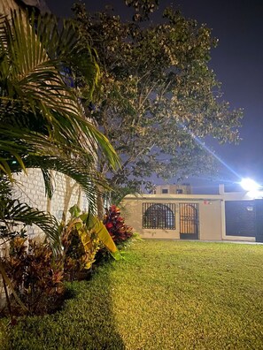 Un césped bien cuidado, un edificio con portón cerrado y un árbol de follaje denso.