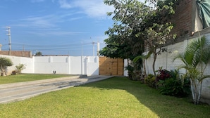 A residential area with a paved driveway, a white fence, and a brick building with a wooden door.