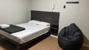 A bed with a dark headboard, a bedside table, a black bean bag chair, and a wall-mounted phone.
