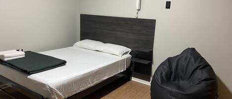 A bed with a dark headboard, a bedside table, a black bean bag chair, and a wall-mounted phone.
