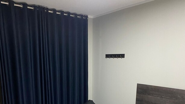 Una habitación de hotel con cama, un sillón tipo bean bag, una mesita de noche y una cortina oscura.