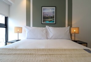 Ein Hotelzimmer mit einem Bett, zwei Nachttischlampen, einem gerahmten Bild an der Wand und einem Fenster.