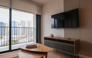 A modern living room with a large window, a flat-screen TV, a wooden table, and a built-in TV stand. - w* | Scenic 2BR w/ Balcony & View in Miraflores (Miraflores)