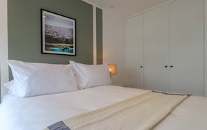 A neatly made bed with white linens, a framed picture on the wall, and a wardrobe with two doors. - w* | Scenic 2BR w/ Balcony & View in Miraflores (Miraflores)