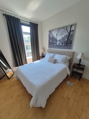 A bedroom with a large bed, a nightstand, a lamp, and a window with curtains. - Luxurious & Spacious Stay in the Heart of Montreal (Montréal)