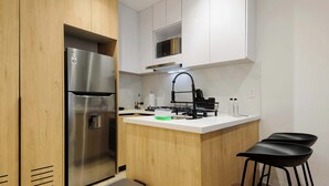 A modern kitchen with a stainless steel refrigerator, wooden cabinetry, a white countertop, a black faucet, and two black bar stools. - w* | Amazing 2BR in the Heart of Roma Sur (Ciudad de México)