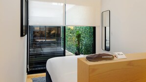 A modern hotel room with a large window, a bed, a wooden dresser, and a mirror. - w* | Amazing 2BR in the Heart of Roma Sur (Ciudad de México)