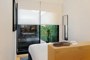 Ein modernes Hotelzimmer mit großem Fenster, einem Bett, einer Holzkommode und einem Spiegel.