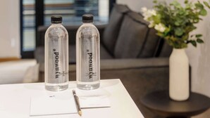 Two clear water bottles with labels on a white table in a modern room with a grey sofa and a vase with white flowers. - w* | Amazing 2BR in the Heart of Roma Sur (Ciudad de México)