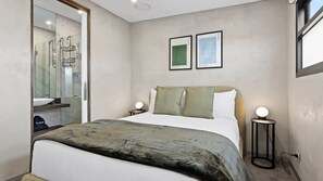 Ein modernes Schlafzimmer mit Bett, Nachttischlampen, einem Spiegel und Kunstwerken an der Wand.