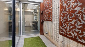 A modern bathroom with a glass door, a shower area, and a decorative metal panel. - Corten Haus South Urban Retreat (South Melbourne)