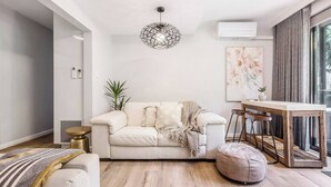 Un salon moderne avec un canapé blanc, un pouf rond, une table basse en bois et un luminaire suspendu.