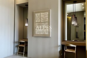 Un intérieur moderne au design minimaliste, agrémenté d’une œuvre d’art abstraite accrochée au mur, d’un espace détente avec un banc et un fauteuil, et d’un grand miroir qui reflète la pièce.