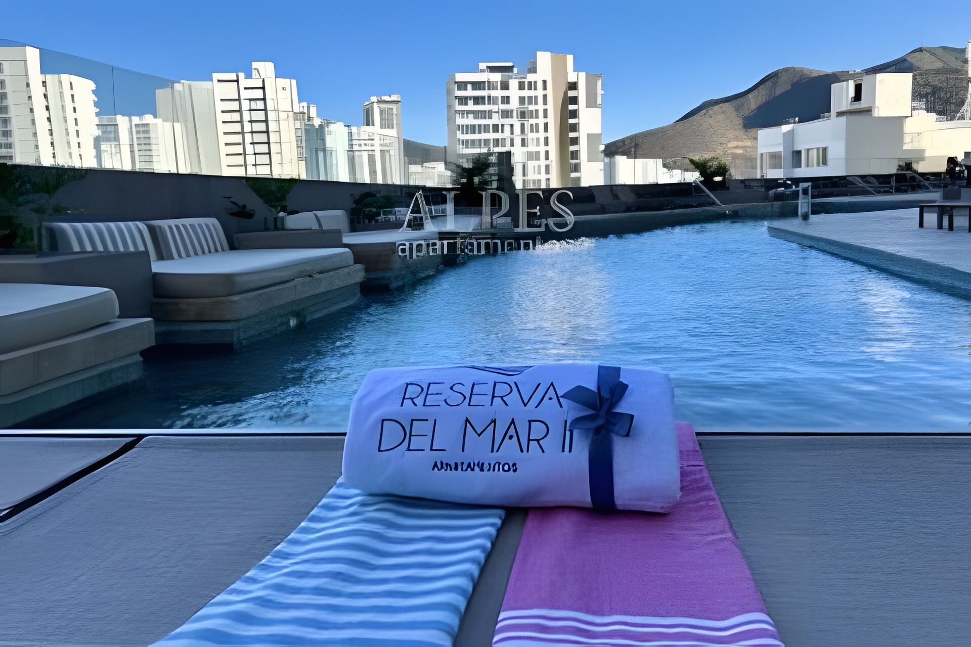 A poolside area with a towel labeled 'RESERVA DEL MAR' and a cityscape in the background.