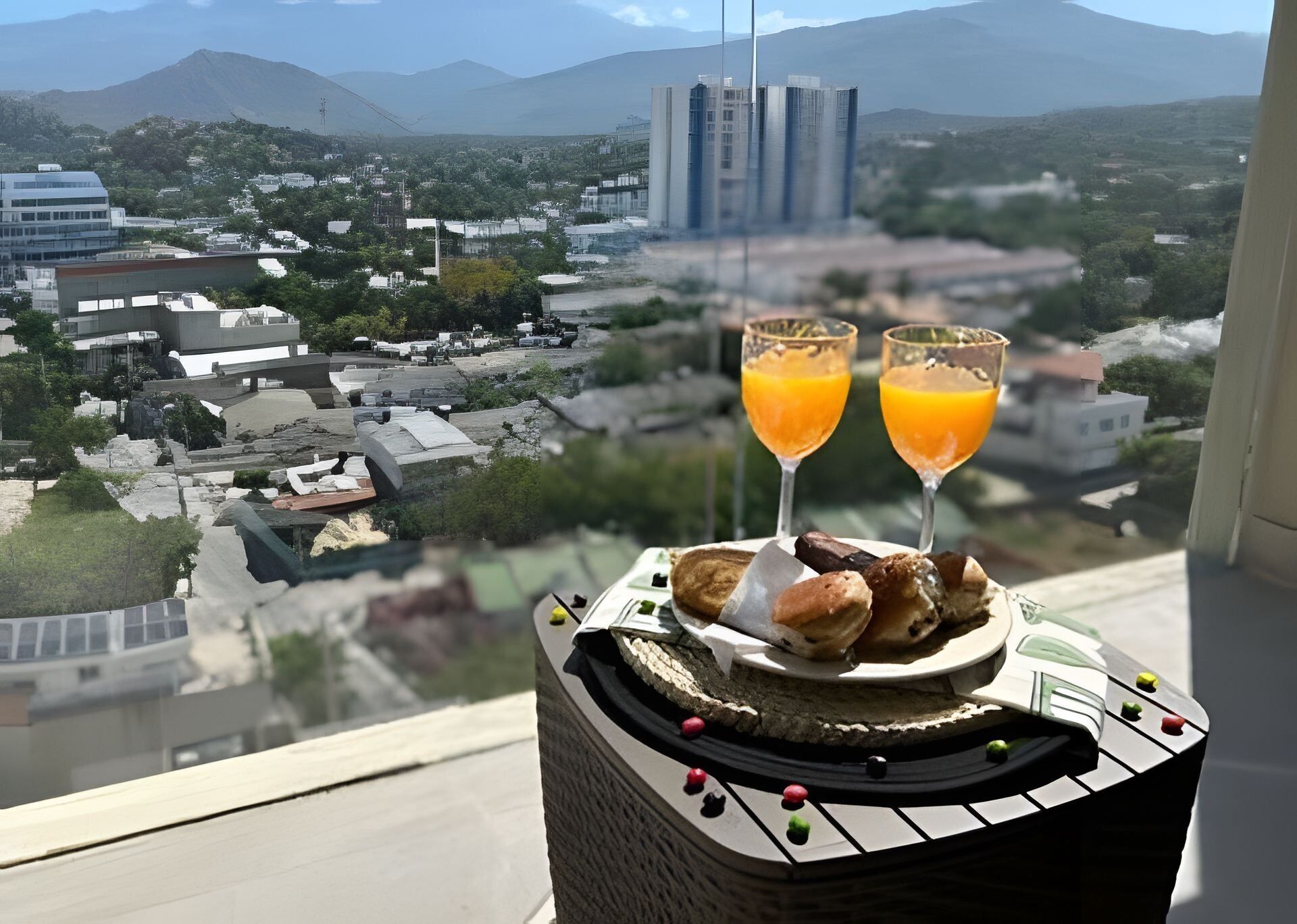 A balcony with a view of a cityscape, two glasses of orange juice, and a plate of food.