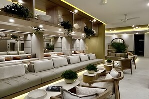 Un salon moderne avec un canapé, des fauteuils et une table basse. Des plantes et des objets décoratifs sont disposés sur des étagères.