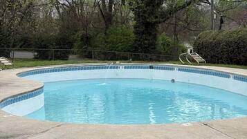 A circular swimming pool with a tiled edge, surrounded by grass and trees.
