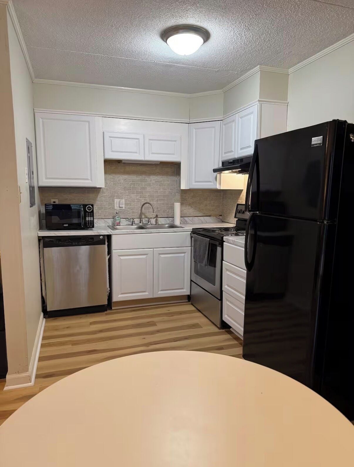 A kitchen with white cabinets, a black refrigerator, a microwave, a dishwasher, and a stove.