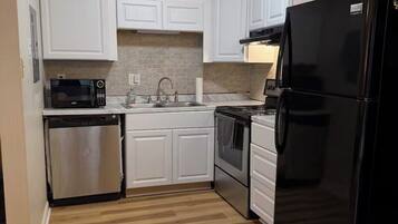 A kitchen with white cabinets, a black refrigerator, a microwave, a dishwasher, and a stove.