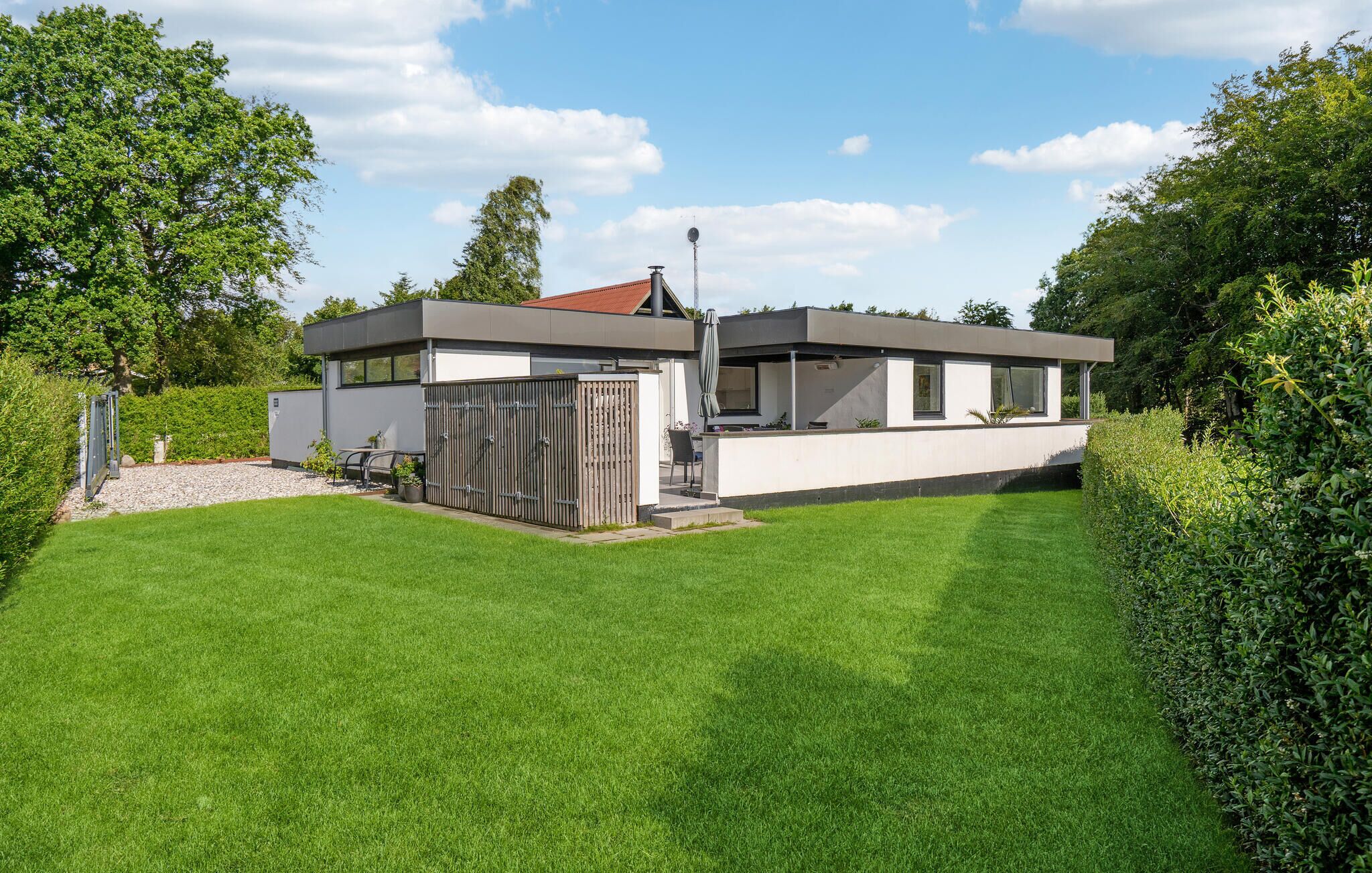 Une maison moderne à deux étages, dotée d’un toit plat, d’une cour arrière clôturée et d’une pelouse bien entretenue.