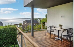 Une terrasse en bois avec une table et des chaises, donnant sur une étendue d’eau.