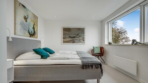 Ein modernes Schlafzimmer mit einem Bett, einem Gemälde, einem Fenster und einem Sessel.
