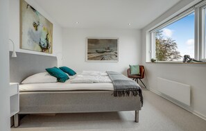 Ein modernes Schlafzimmer mit einem Bett, einem Gemälde, einem Fenster und einem Sessel.