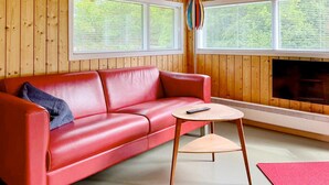 Un sofá de cuero rojo, una mesita de madera y una chimenea en una habitación con paredes de madera y ventanas grandes.