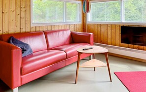 Ein rotes Ledersofa, ein kleiner Holztisch und ein Kamin in einem Raum mit Holzwänden und großen Fenstern.