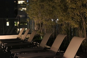 Reihenweise angeordnete Lounge-Stühle im Freien, mit einer Silhouette aus hochwachsenden Bambuspflanzen im Hintergrund.