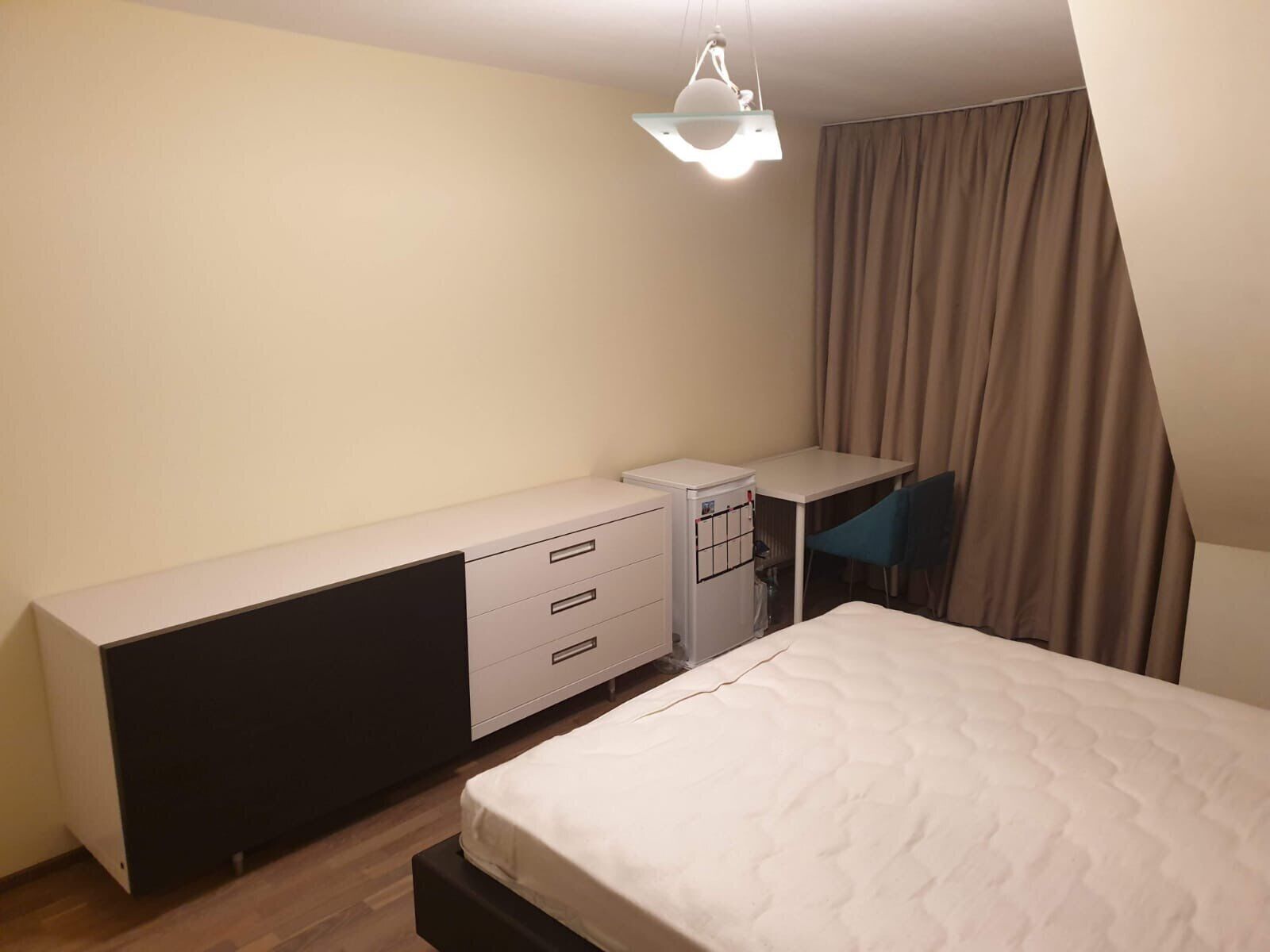Un dormitorio con cama, escritorio, silla, armario e iluminación colgante.