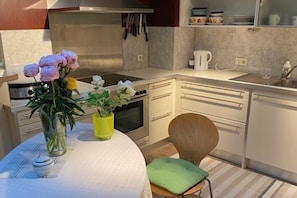 A kitchen with white cabinets, a stove, a sink, and a chair with a green cushion. - Apartment Sleeps 6 with Garden & Balcony (Wien)