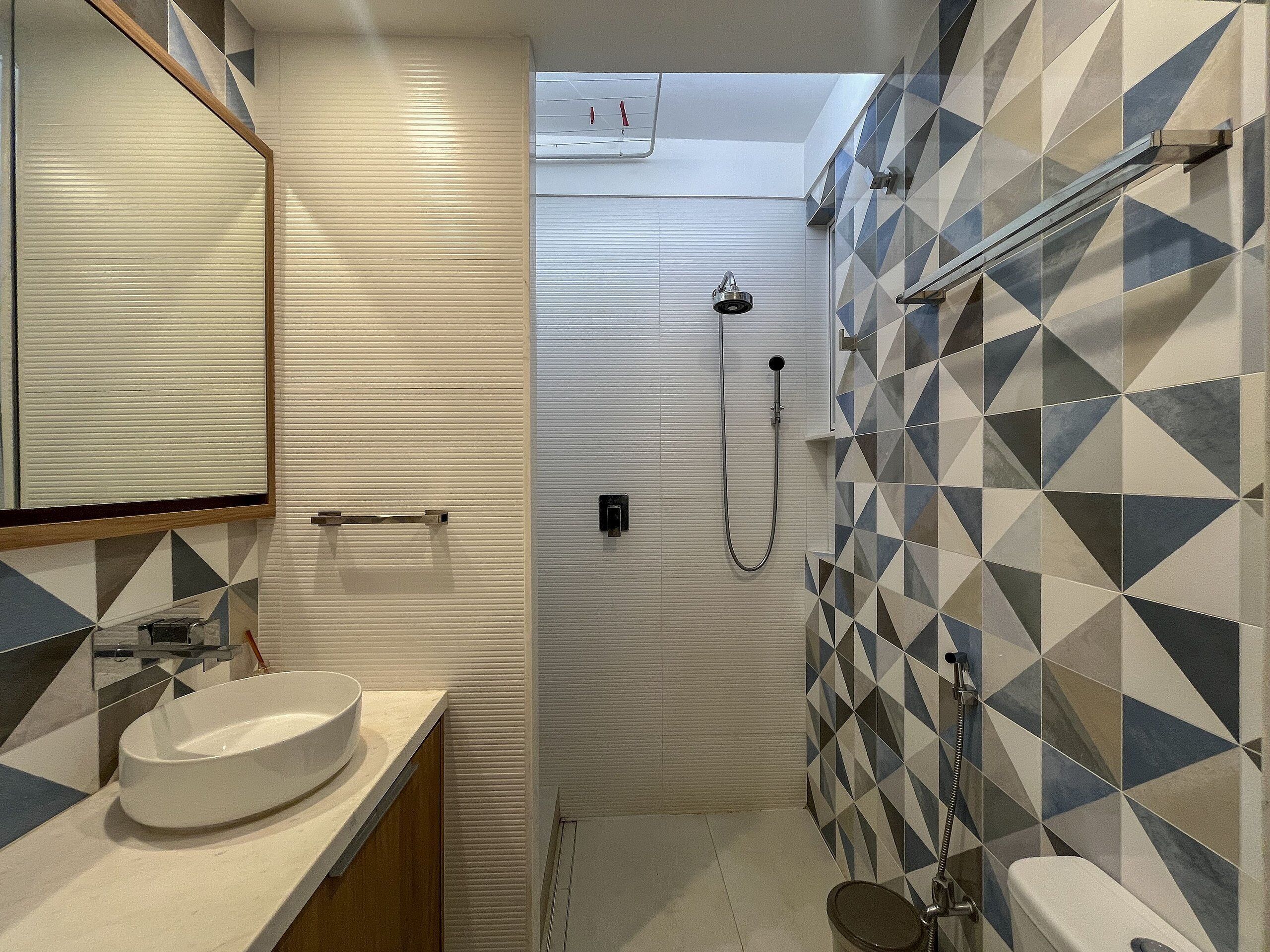 Ein Badezimmer mit einem weißen Waschbecken, einer Toilette und einer Dusche mit geometrischem Fliesenmuster.