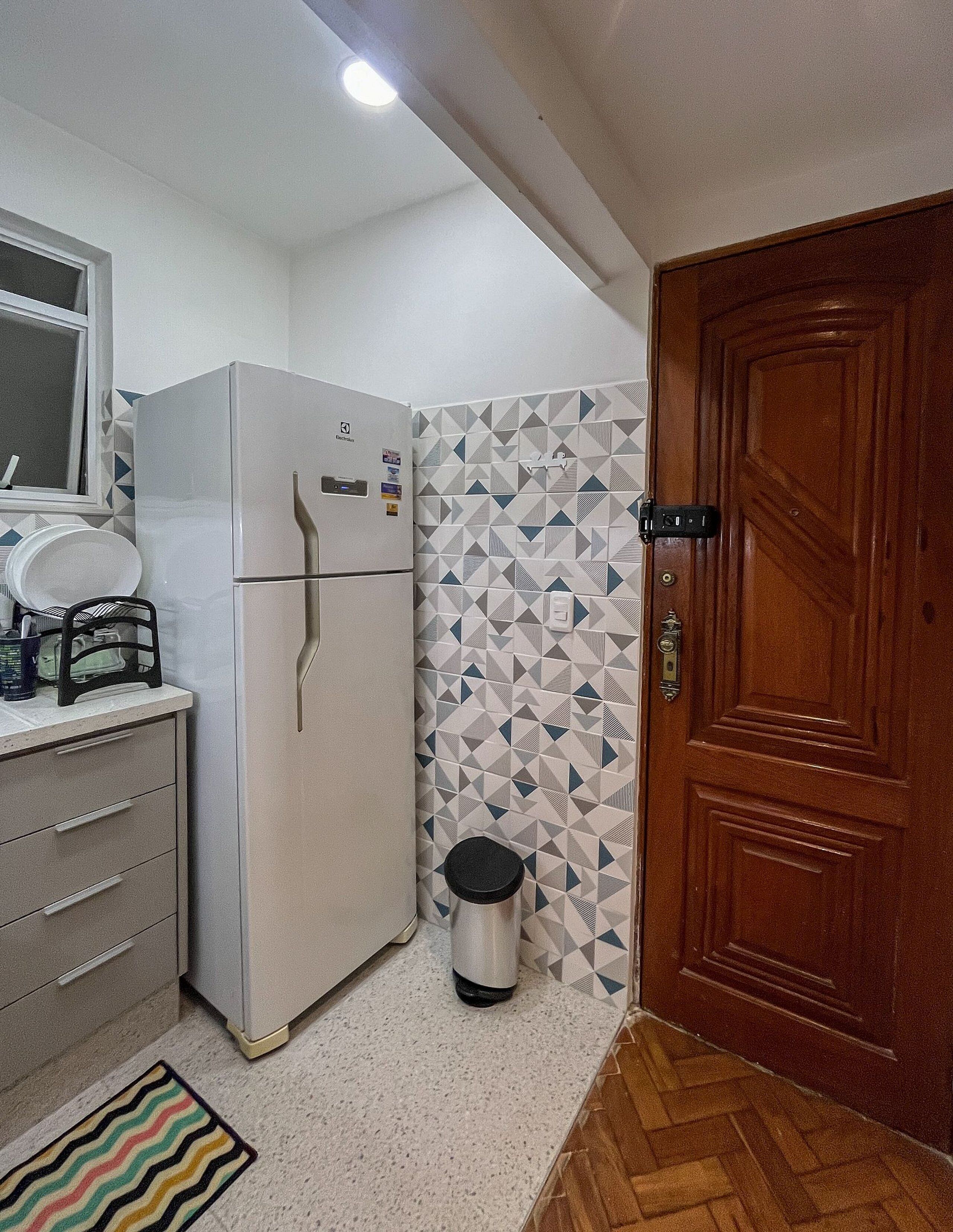 A compact kitchen with a refrigerator, a wooden door, and a patterned wall.