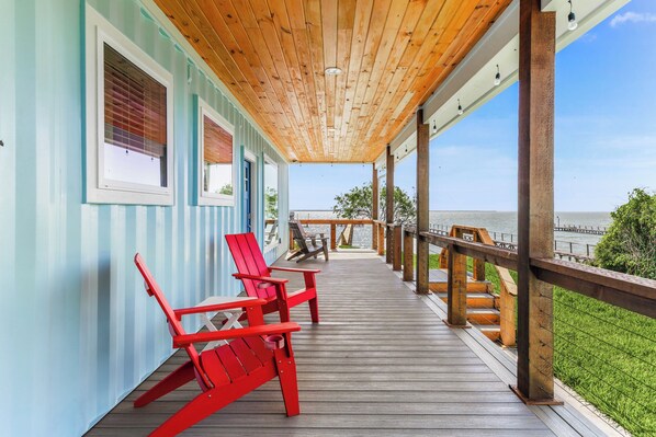A wooden deck with red Adirondack chairs, a view of the water, and a wooden railing.