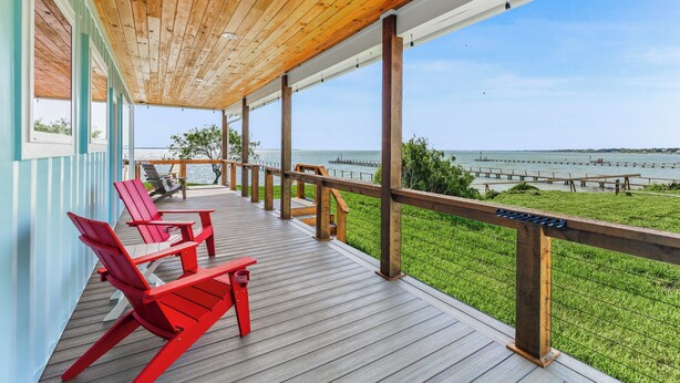 Una terraza de madera con sillas Adirondack rojas y vista al agua.