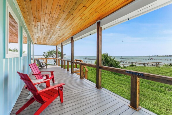Una terraza de madera con sillas Adirondack rojas y vista al agua.