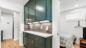 A modern kitchen with dark green cabinets, a white countertop, and a brick backsplash.