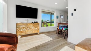 A modern living room with a flat-screen TV, wooden cabinet, and colorful chairs.