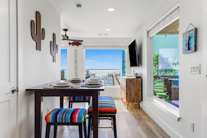 Un comedor con vista al mar, una mesa de madera, sillas coloridas y un televisor en la pared.