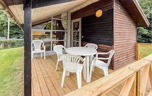 Una baita di legno con una veranda, sedie di plastica bianca e un tavolo rotondo.