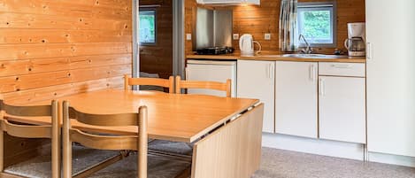 A compact kitchen with wooden walls, a dining table with chairs, a built-in stove, and a window with curtains.